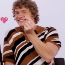 Man making a finger heart gesture with a pink heart icon floating nearby.