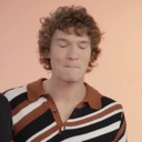 Man with curly hair making a skeptical, pursed-lip facial expression.
