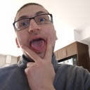 Man with glasses sticking his tongue out and touching his chin playfully.