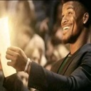 A man smiling broadly while holding a paper that emits a bright golden glow.