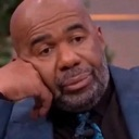 Steve Harvey resting his head on his hand with a skeptical and bored expression.