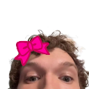 Person with curly hair wearing a bright pink bow looking directly into the camera.