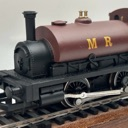 A brown and black model steam locomotive sits on wooden train tracks.