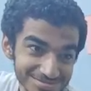 A man with a dark, curly-haired head and a mischievous, knowing smirk on his face.