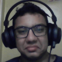 A man wearing glasses and headphones looking at the camera with a squinted, unimpressed expression.