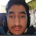 A young man with headphones looks directly into the camera with a neutral, serious expression.