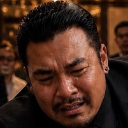 A man with a mustache and earring wearing a suit has a pained, crying expression.