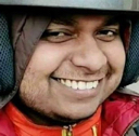 A man wearing a helmet with a wide, mischievous, and smug smile.