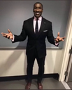 Shannon Sharpe in a black suit standing with his arms spread wide in a gesture of confusion.