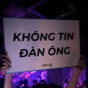 Hands holding up a white sign with black text that reads Khong Tin Dan Ong in a dark, purple-lit club environment.