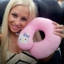 A blonde woman smiling while holding a pink Hello Kitty neck pillow.
