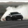 A black car drifting on a track surrounded by a large cloud of white tire smoke.