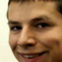 Man with a close-cropped face showing a subtle, mischievous smirk.