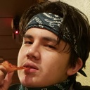 A young man wearing a dark bandana looks at the camera with a skeptical, judgmental expression while holding a snack.