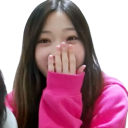A young woman in a pink hoodie covers her mouth with her hand while giggling.
