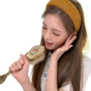 A young woman with a yellow headband singing enthusiastically into a hairbrush.