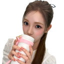 A young woman with brown hair holding a white tumbler and sipping from it while looking directly at the camera.