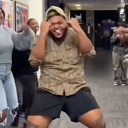 A man wearing a tan shirt and black shorts dancing enthusiastically with his hands near his head.