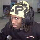 A man wearing a yellow and black patterned beanie and headphones looking sideways with a skeptical expression.
