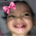 A child with a pink bow making a wide, chaotic, toothy grin at the camera.