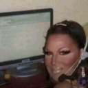 A person with a headset looking at the camera in front of a computer screen.
