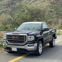 A black GMC pickup truck parked on the side of a road with a mountain in the background.