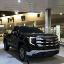 A black GMC pickup truck parked under the bright lights of a gas station canopy.