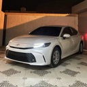 White sedan parked in a garage with headlights on.