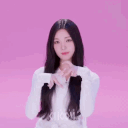 A young woman with long dark hair performs a series of heart-shaped hand gestures against a pink background.