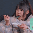 A young girl with a ponytail eating from a bowl with a spoon, looking happy and focused.