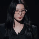 A woman with dark hair and glasses gives a thumbs-up gesture while looking directly at the camera.