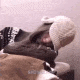A person wearing a textured winter hat and sweater resting their head on a soft surface.