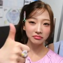 Young woman giving a deadpan thumbs-up gesture while wearing a pink shirt.