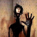A dark, spindly creature with a pale face reaching out with a long hand against a patterned wall.