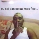 A man holds his index finger to his lips in a shushing gesture while looking at the camera.