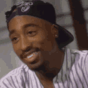 Tupac Shakur laughing with a wide smile while wearing a black bandana.