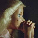 A blonde doll with a tear on its cheek and hands clasped in prayer.