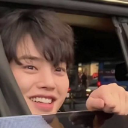 A person smiling and waving from a car window.