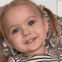 A young girl with pigtails giving a mischievous, knowing smirk.