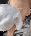 A toddler with their face buried in a large, fluffy ball of white cotton candy.
