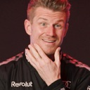 Man with a mischievous grin touching his chin in a thoughtful gesture.