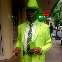 Man wearing a bright neon green suit and matching hat standing in a street.