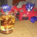 Optimus Prime action figure sitting behind a glass of amber liquid.