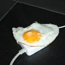 A fried egg sitting on top of a white power adapter plug against a dark background.