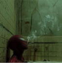 Spider-Man sits in a dark, tiled bathroom smoking a cigarette with a weary expression.