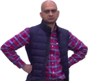 A bald man wearing a plaid shirt and vest standing with his hands on his hips looking disappointed.