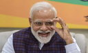 Narendra Modi smiling while adjusting his glasses with his right hand.