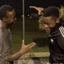 Two friends laughing and interacting playfully with their hands in a candid, low-light setting.