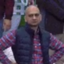 A man with a shaved head wearing a plaid shirt and vest stands with his hands on his hips looking extremely disappointed.