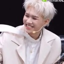 A young man with blonde hair smiling brightly while wearing a white jacket.